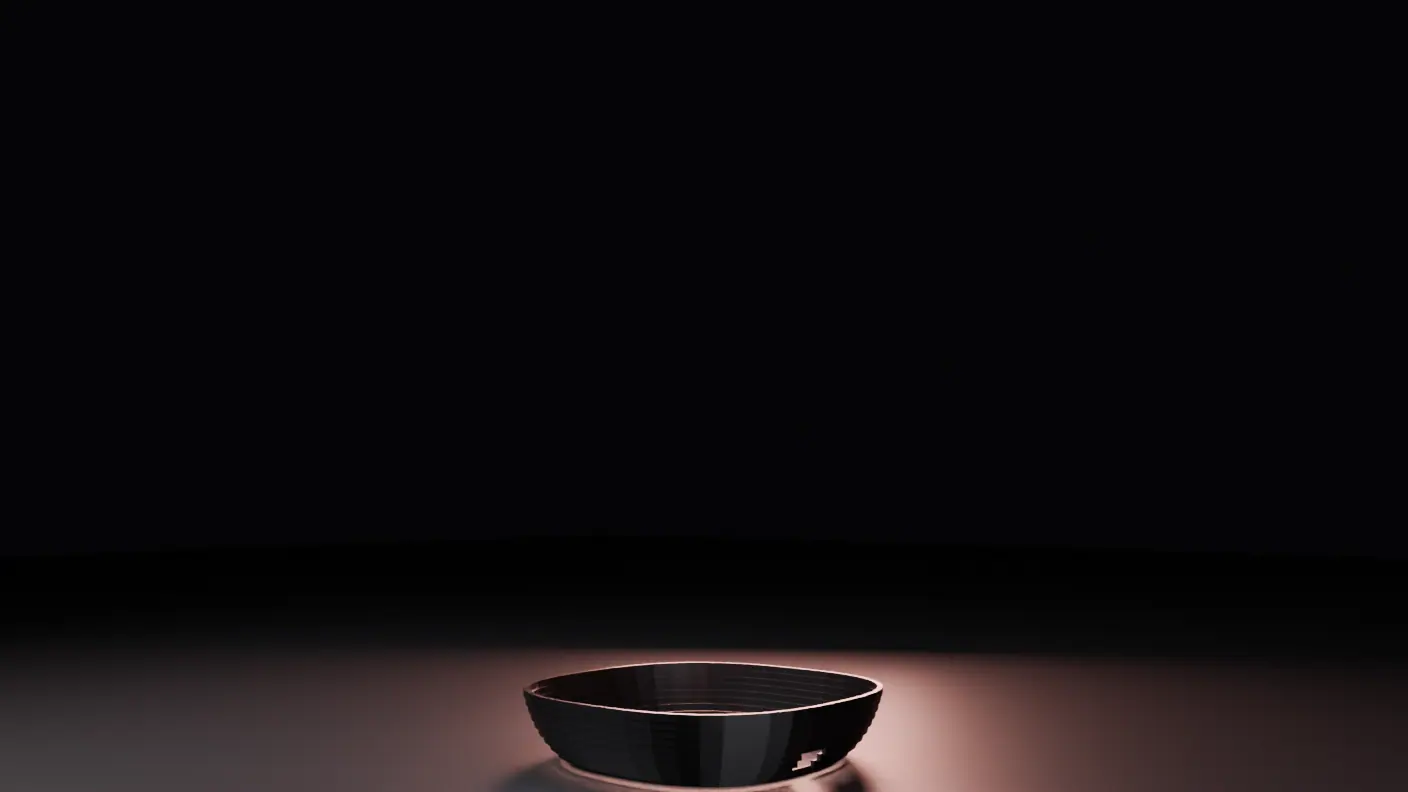 A shallow ribbed bowl resting alone on a softly lit floor in a dark room — the machine's base, before anything is added to it.